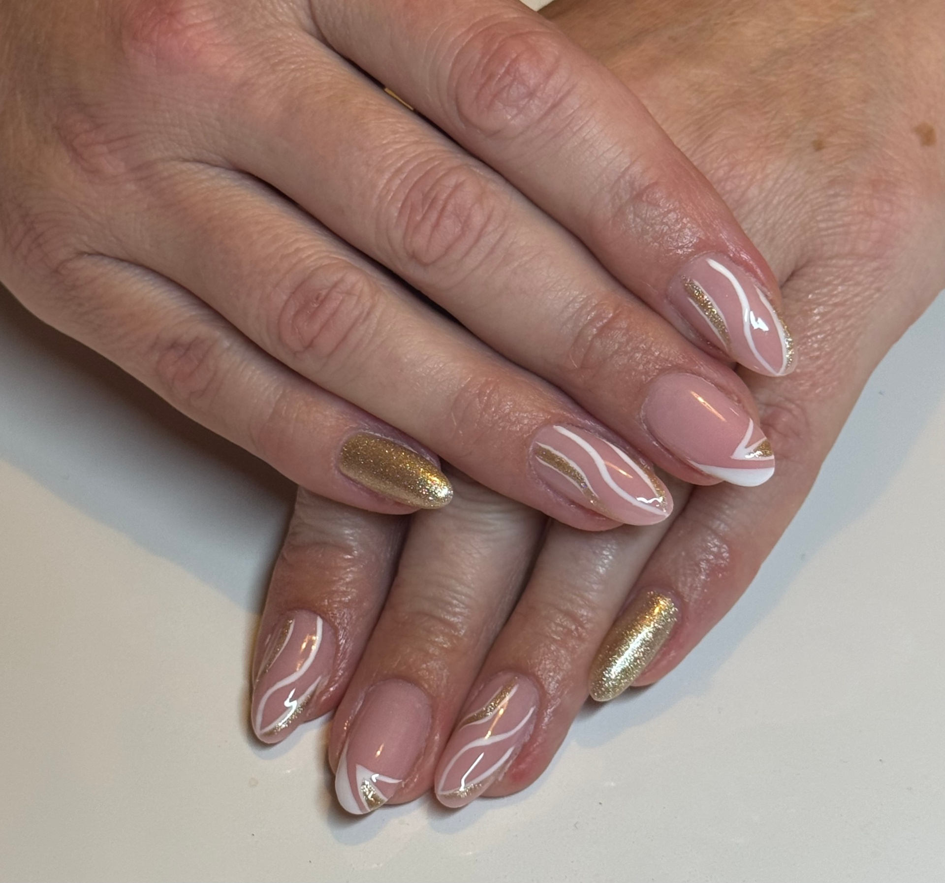 Nude almond nails with gold shimmer swirls and one full gold accent